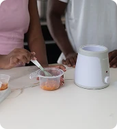 Parents preparing baby food using the Snookums bottle and food warmer